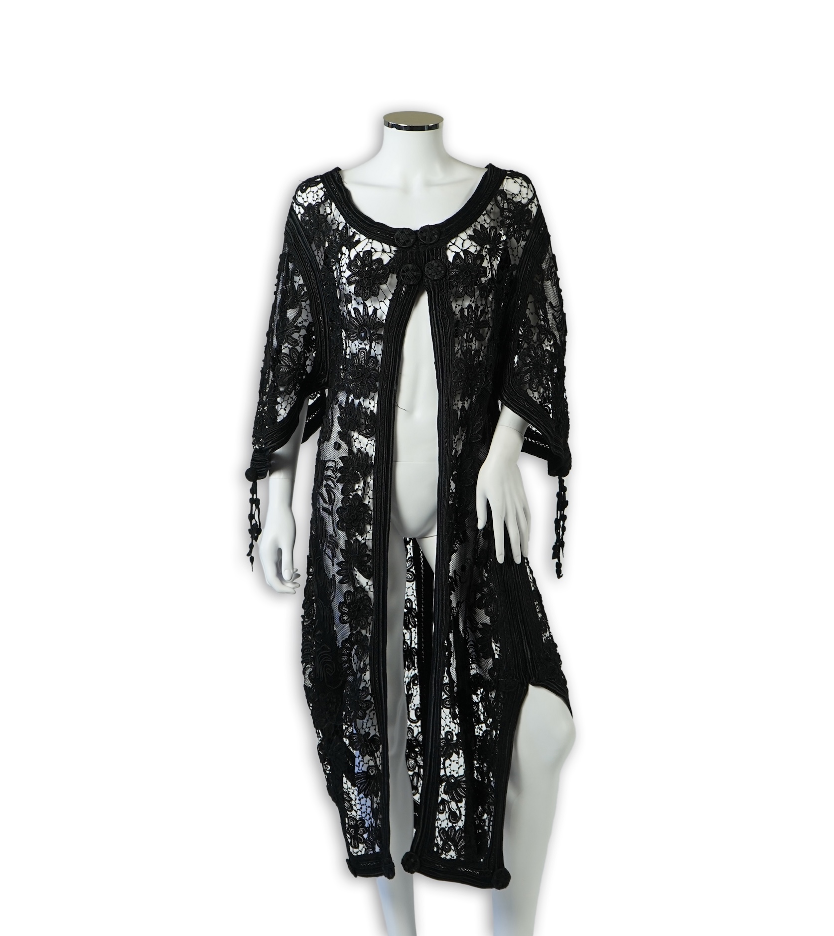 A late 19th century stylish ornate black silk tape lace evening coat/dress. Designed with a wide open neck, short bell sleeves with long tassels, four large buttons at the front and tails at the front and back. 130cm lon